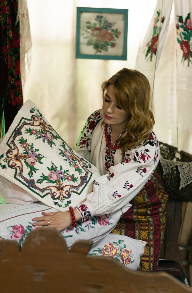 Ukrainian woman in folk attire holding an embroidered pillow indoors.